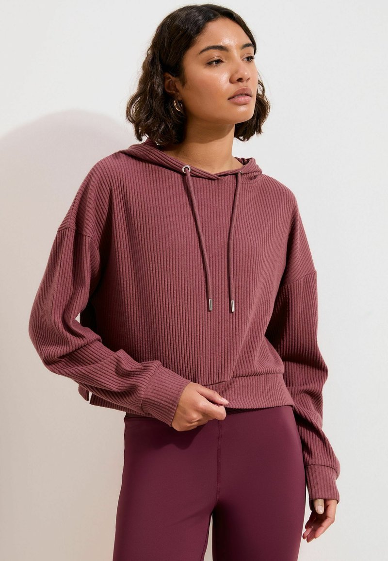 Ribstrikket, cropped hættetrøje i støvet rosa med snøre i hætten, lange ærmer og løs pasform. Brugt med matchende, tætsiddende leggings.
