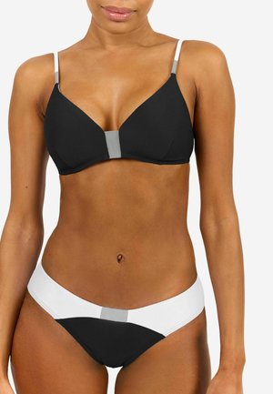 Frau, die einen schwarz-weißen Colorblock-Bikini mit grauen Akzenten vor einem schlichten weißen Hintergrund trägt.