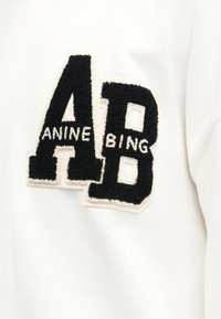 Μαύρα γράμματα με υφή «A» και «B» με άσπρο κείμενο «ANINE» μέσα στο A και «BING» μέσα στο B σε λευκό υφασμάτινο φόντο.