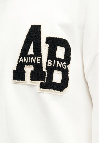 Juodos tekstūruotos raidės „A“ ir „B“ su baltais užrašais „ANINE“ raidės „A“ viduje ir „BING“ raidės „B“ viduje, ant balto audinio fono.