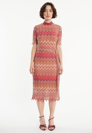 Knielanges, tailliertes Kleid mit einem Zickzackmuster in Rot-, Orange- und Beigetönen. Hat einen hohen Kragen und kurze Ärmel sowie einen Bindegürtel.