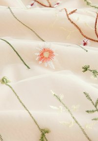 Tissu blanc transparent avec des tiges et des feuilles vertes, et des fleurs brodées orange et blanches dispersées sur la surface.