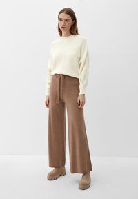 Cremefarvet ribstrikket sweater, brune bukser med vide ben og bånd i taljen, samt beige platform støvler præsenteret mod en minimalistisch hvid baggrund.