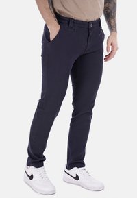 Chinos blu navy con vestibilità slim, realizzati in un leggero tessuto misto cotone. Presentano tasche anteriori e zip, abbinati a sneakers bianche.