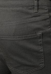 Zwarte denimjeans hebben een achterzak met contrasterende stiksels en een gladde, iets gestructureerde stof. Het ontwerp sluit strak aan.