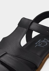 Μαύρο δερμάτινο σανδάλι με κλειστή μύτη, λουρί στον αστράγαλο και καφέ σόλα, που εμφανίζει υφή υλικού και λεπτομέρειες ραφής.