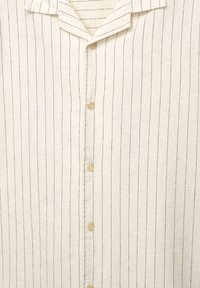 Chemise beige clair boutonnée avec des rayures verticales foncées, dotée d'un col et de boutons naturels. Tissu doux et texturé.