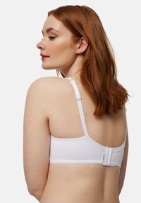 Sostén blanco con textura suave, tirantes ajustables y cierre de gancho en la parte posterior. Cuenta con un borde festoneado a lo largo de los bordes.