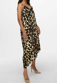 Schwarz-braun gemustertes Leoparden-Kleid mit Spaghettiträgern, fließender Silhouette und asymmetrischem Saum. Modell kombiniert mit hautfarbenen High Heels.