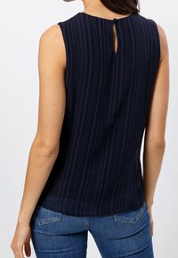 Mörkblå ärmlös topp med vertikala ränder och en liten nyckelhålsknäppning bak. Lättviktsmaterial med en slät textur.