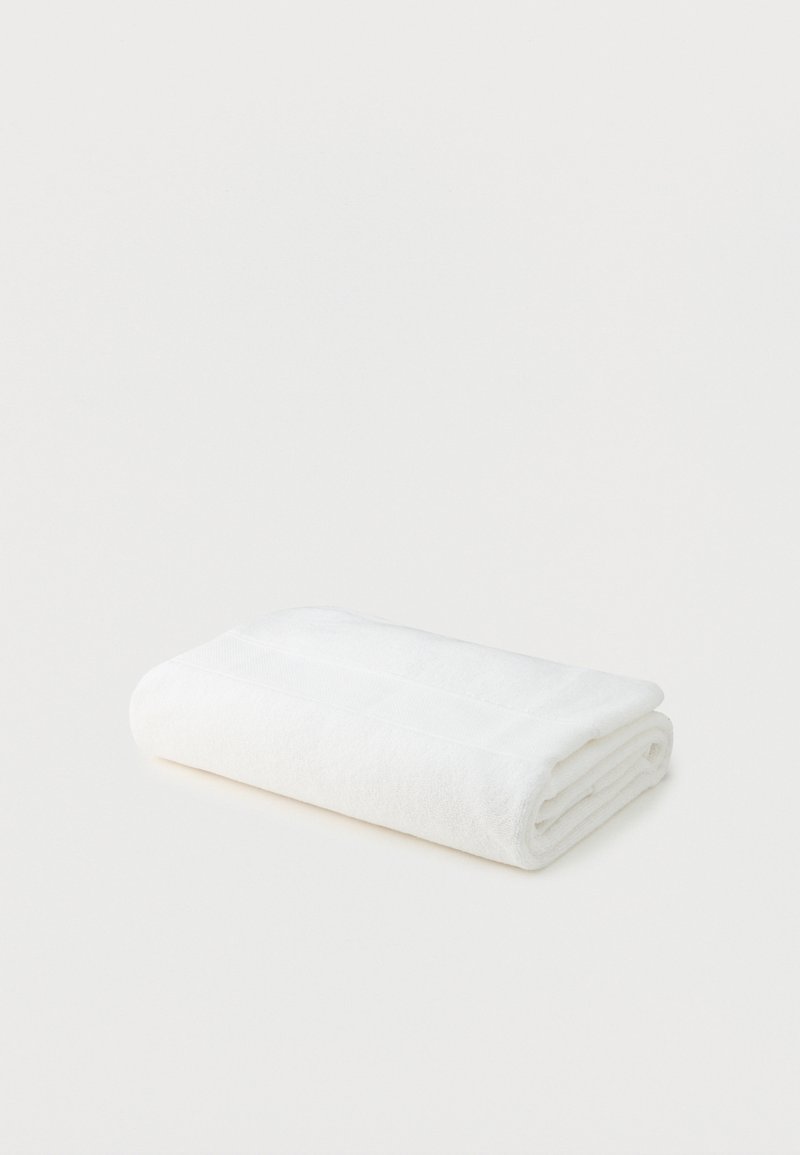 Λευκή βαμβακερή πετσέτα μπάνιου διπλωμένη, τοποθετημένη πάνω σε απλό λευκό φόντο.
