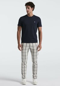 Marineblauwe crew-neck T-shirt gecombineerd met crèmekleurige geplaid broek met marineblauwe lijnen. Model draagt witte sneakers en staat tegen een effen achtergrond.