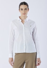 Camicia bianca con bottoni, maniche lunghe, dotata di un piccolo logo ricamato sul lato sinistro del petto e un design del collo classico. Tessuto a trama.