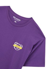 T-shirt viola a maniche corte con una vestibilità rilassata, scollatura rotonda e una grafica di un orso con un banner giallo con la scritta "REGOLI" sul petto.
