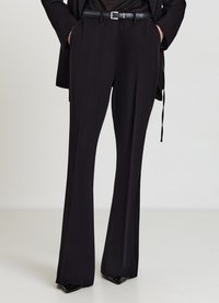 Pantalon noir sur mesure avec une coupe évasée, une texture lisse et une taille ajustée. Associé à une ceinture noire avec une boucle argentée.