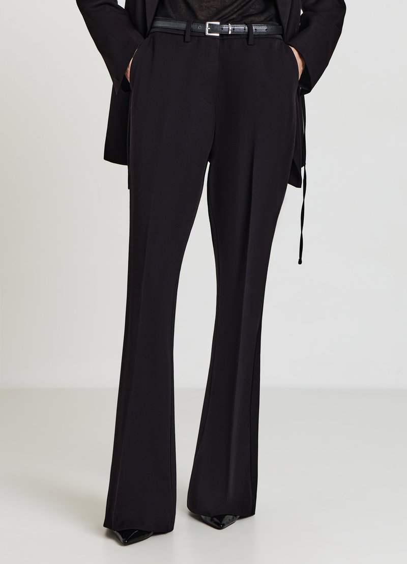 Pantalon noir sur mesure avec une coupe évasée, une texture lisse et une taille ajustée. Associé à une ceinture noire avec une boucle argentée.