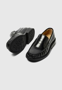 Sorte lærloafers med en sydd aksent, rund tå og teksturert elastisk trim. Gummisålen har sirkulære gripe mønstre.