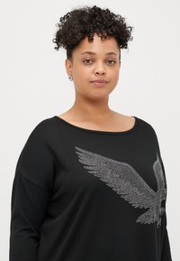 Schwarzer Sweatshirt mit einem weiten Ausschnitt, langen Ärmeln und einem metallisch silbernen Adlerdesign aus kleinen Nieten auf der Vorderseite.