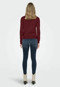 Maglione a maglia bordeaux abbinato a jeans scuri, con un design aderente. Calzature composte da stivaletti beige alla caviglia con una forma del tacco distintiva.
