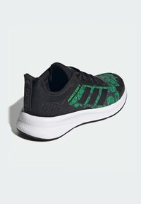 Czarno-zielone buty sportowe z fakturowaną cholewką ozdobioną geometrycznym wzorem, białą śródstopą i czarną podeszwą zewnętrzną.