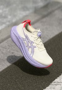 Hardloopschoen met een crèmekleurig bovenwerk, paarse spikkels op de middenzool, rode accenten en een rond logo op de tong. Lichtgewicht ontwerp voor prestaties.