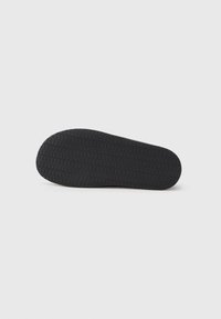 Black rubber shoe sole featuring a textured pattern with small grips, providing traction and durability. Rounded shape with a smooth edge.
