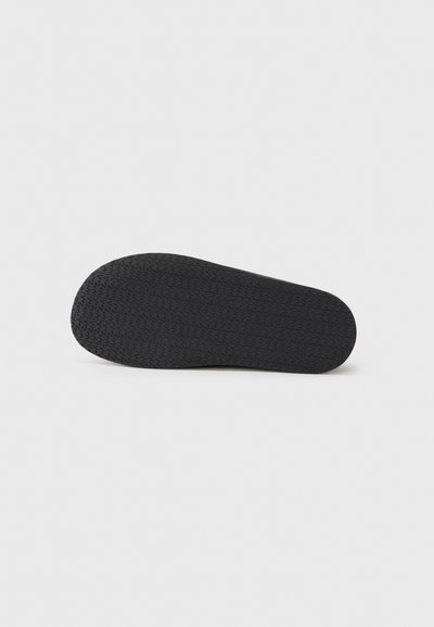 Semelle de chaussure en caoutchouc noir présentant un motif texturé avec de petites accroches, offrant traction et durabilité. Forme arrondie avec un bord lisse.