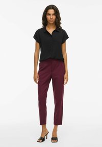 Zwarte korte-mouwen overhemd met knopen, gecombineerd met bordeauxrode slim-fit broek en zwarte open teen haksandalen. Zachte stoftextuur.