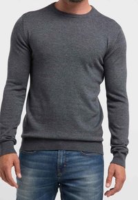 Grauer Strickpullover mit langen Ärmeln und rundem Ausschnitt, mit gerippten Bündchen und Saum, getragen über blauer Jeans.