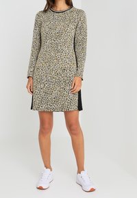 Robe à manches longues imprimée léopard en beige et noir, dotée d'un col rond et de panneaux latéraux. Portée avec des baskets blanches.