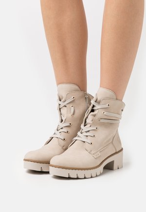 Bottines beige en cuir lisse, dotées d'un système de laçage, d'une fermeture à glissière latérale et d'une semelle épaisse à rainures pour une meilleure adhérence.
