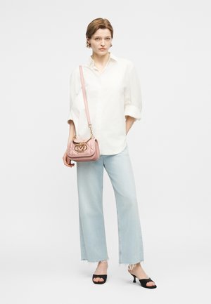 Γυναίκα με λευκό πουκάμισο με κουμπιά, ανοιχτό μπλε τζιν παντελόνι με φαρδιά πόδια και φθαρμένα τελειώματα, μαύρα σανδάλια με τακούνι και ροζ τσάντα ώμου με χρυσό λογότυπο.