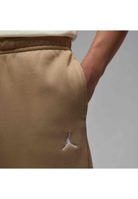 Beige sweatpants with a smooth texture, featuring an elastic waistband and a white embroidered logo on the left thigh.