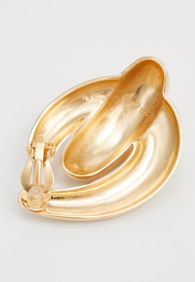 Gouden broche met een glad, gebogen ontwerp en een glanzende metalen afwerking. Beschikt over een veilige sluitmechanisme en een onderscheidende, vloeiende vorm.