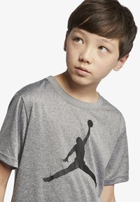 Grå t-skjorte med korte ermer laget av myk stoff. Har et stort svart silhuett av en basketballspiller på forsiden.