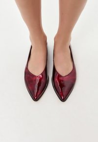 Ballerines en cuir verni rouge à bout pointu avec une finition brillante et un talon bas. Le design présente une découpe en V profonde à l'avant pour un look élégant.