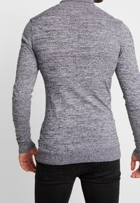 Pull à manches longues pour homme, tricot texturé gris moyen, coupe ajustée, poignets et ourlet côtelés, minimaliste branding sur la couture latérale.