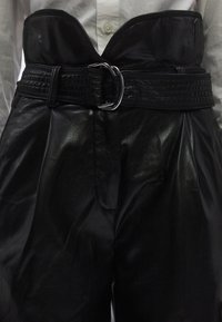 Svarta högmidjade byxor i läder med en bred midjeband med texturerad design och silver spänne, som visar ett slätt, glänsande material.