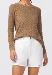 Sweter dziany w jasnobrązowym kolorze z teksturowanym wzorem w romby, zestawiony z białymi szortami jeansowymi z postrzępionym brzegiem.