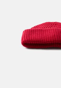 Czerwona dziergana czapka beanie o prążkowanej teksturze, z podwinięciem na dole i gładkim wierzchem, wykonana z miękkiego, ciepłego materiału.