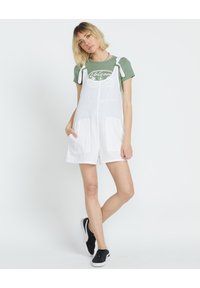 Abito in cotone bianco con bretelle regolabili, due tasche frontali e una T-shirt verde a collo rotondo con un disegno al centro.