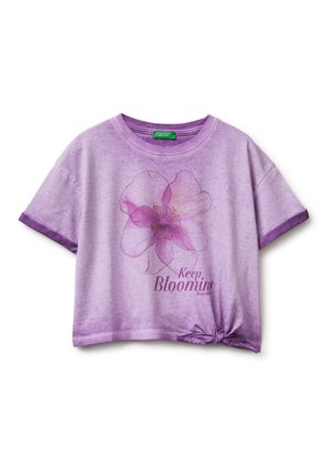 Fioletowa koszula z krótkim rękawem z dużym różowym kwiatowym nadrukiem, napisem „Keep Blooming” oraz supłem na dolnym prawym brzegu.