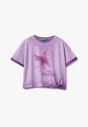 Levandulová košile s krátkým rukávem s velkým růžovým květinovým motivem, textem „Keep Blooming“ a uzlíkem v pravém dolním okraji.