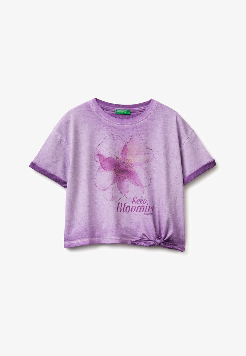 Fioletowa koszula z krótkim rękawem z dużym różowym kwiatowym nadrukiem, napisem „Keep Blooming” oraz supłem na dolnym prawym brzegu.