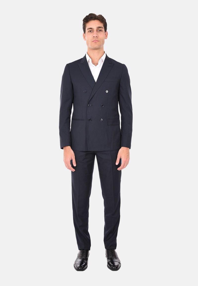 Giacca navy doppiopetto con due bottoni, pantaloni coordinati e scarpe nere da cerimonia. Camicia bianca con colletto sotto. Tessuto morbido.