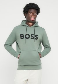 Sudadera verde hecha de un material suave con un gran logo negro "BOSS" en el frente, que cuenta con un bolsillo tipo canguro y capucha con cordón.