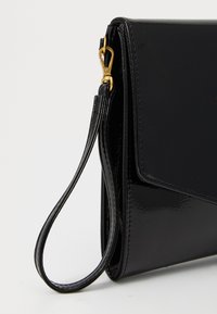 Black patent leather clutch with a curved flap and a detachable wrist strap. Features gold hardware and a smooth, glossy finish.
