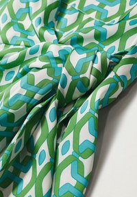 Tissu plié avec un motif géométrique de formes vertes et bleues entrelacées sur fond blanc.