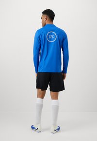 Langærmet blå atletisk tr�øje med "CFC" logo, parret med sorte shorts og hvide knæstrømper, båret med blå og hvide fodboldstøvler.