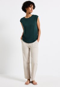 Donkergroen top met korte mouwen van textuurstof en schouderdetails, gecombineerd met beige wijde broek en lichte sandalen.